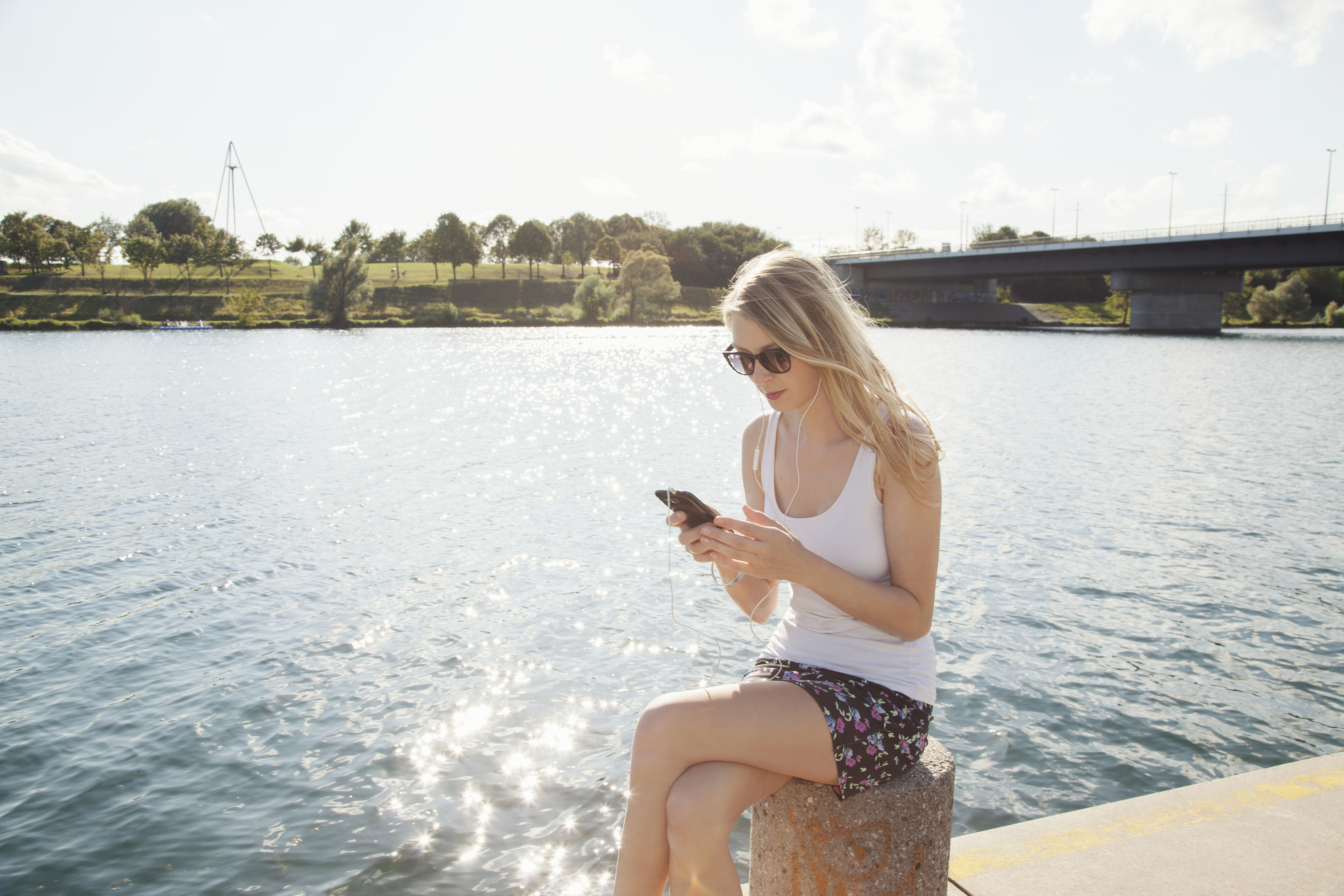 young woman sitting at riverside texting on smartp 2022 03 08 00 06 06 utc